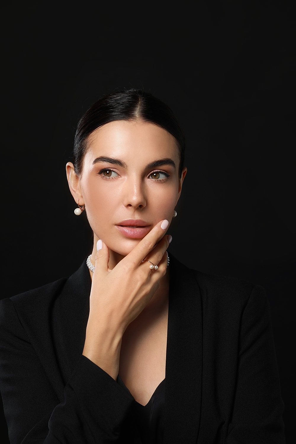 Woman in elegant attire with jewelry on black background.