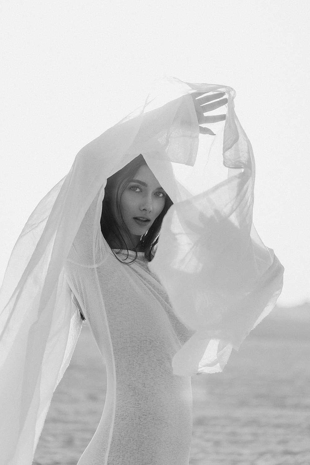 Woman holding sheer fabric on a beach.