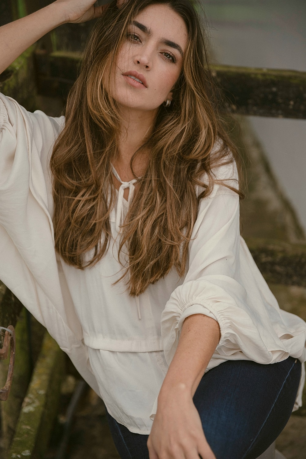Woman with long hair posing by wooden fence.
