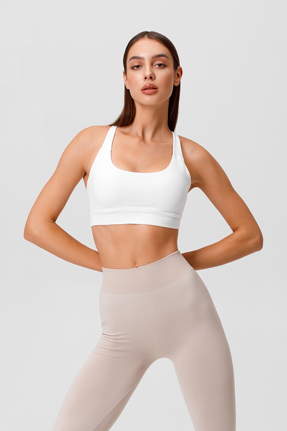 Model wearing white sports bra and beige leggings.