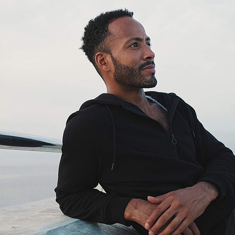 Man sitting outdoors, looking thoughtfully into distance.